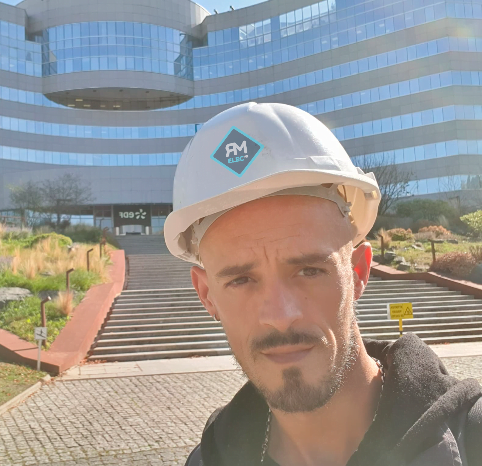 Technicien en casque blanc devant un bâtiment moderne avec façade en verre et logo